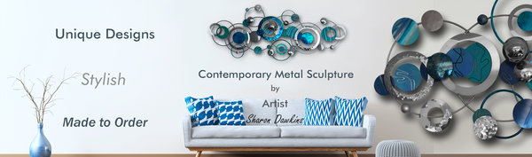 Image of large Blue and shiny Silver artwork, Three dimesional art, reflective textured artwork consisting of  overlapping circles.Wall Art displayed over sofa White sofa with pattered Blue cushions,unique designs,stylish art,custom style art by Artist Sharon Dawkins The Sculpture Room.