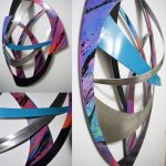Curved metallic sculpture with blue, purple, black, and orange colors mounted on white wall background.