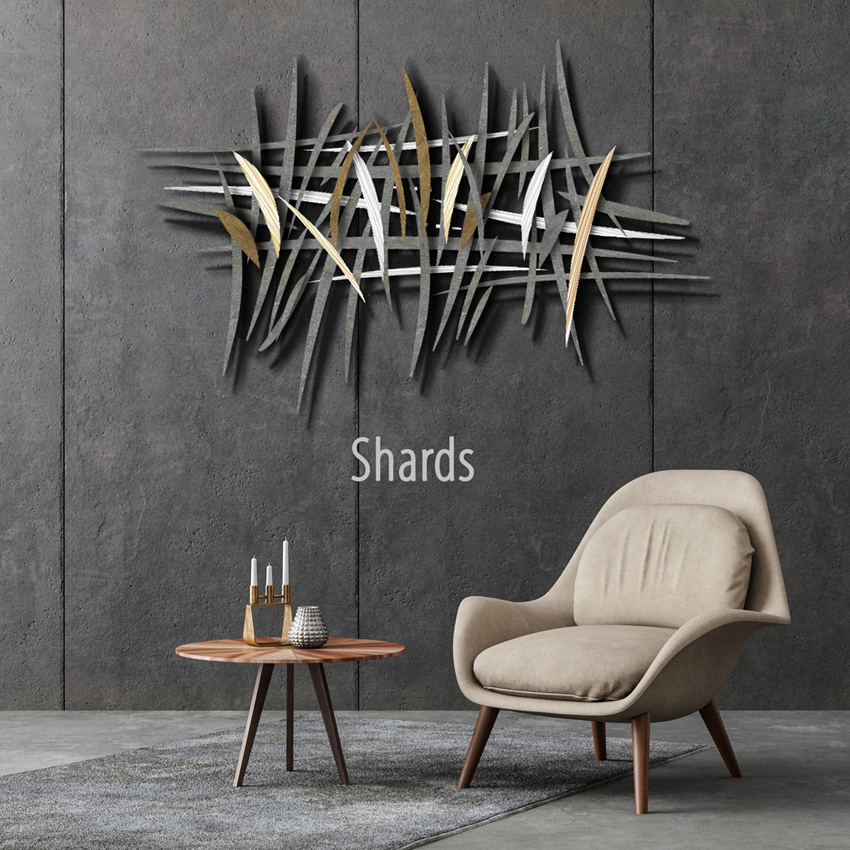 A modern living room with a minimalist design features a comfortable beige armchair next to a small round wooden table with candles and a decorative object. The dark gray textured wall is adorned with a striking abstract metal wall sculpture made of intersecting black, silver, and gold shards. The word "Shards" is displayed below the wall art.