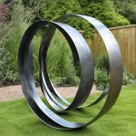 Large stainless steel ribbon sculpture with interwoven curved loops, set on a landscaped garden lawn with lush greenery and wooden fencing