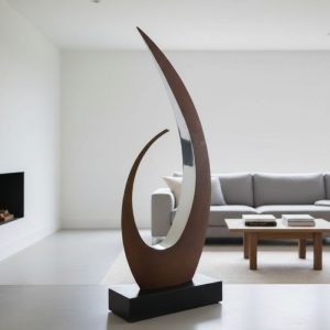 Modern abstract metal sculpture with curved design, displayed in a minimalist living room near gray sofa.