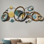 Orbit wall sculpture featuring interlinked circles and spheres in teal, gold, and bronze, displayed above a minimalist sofa