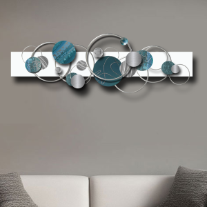 Abstract circular wall art in teal, turquoise, and brushed silver tones, mounted above a minimalist cream sofa. Handmade metal sculpture featuring layered discs and rings.