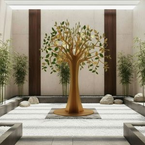 Golden decorative tree sculpture in a modern indoor zen garden with bamboo plants and white stones.
