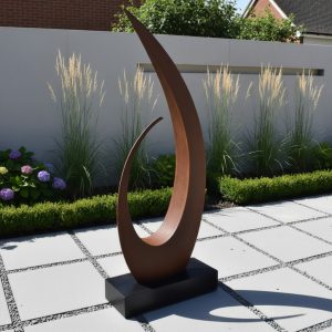 Curved bronze sculpture on black base in landscaped garden with grasses, hedges, paved tiles.