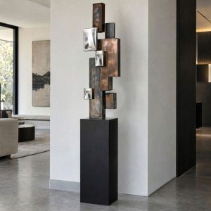 Urban Ascent geometric metal sculpture with rustic patina, visible welds and polished stainless steel, displayed on a black pedestal.